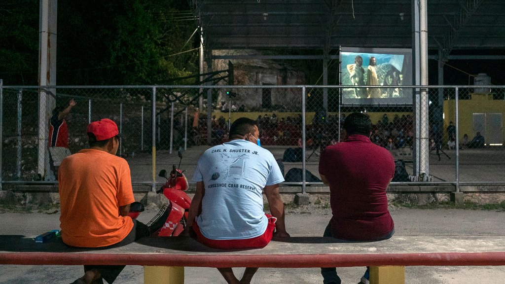 people sitting on bench in the foreground while the Jesus Film plays on a projector in the background