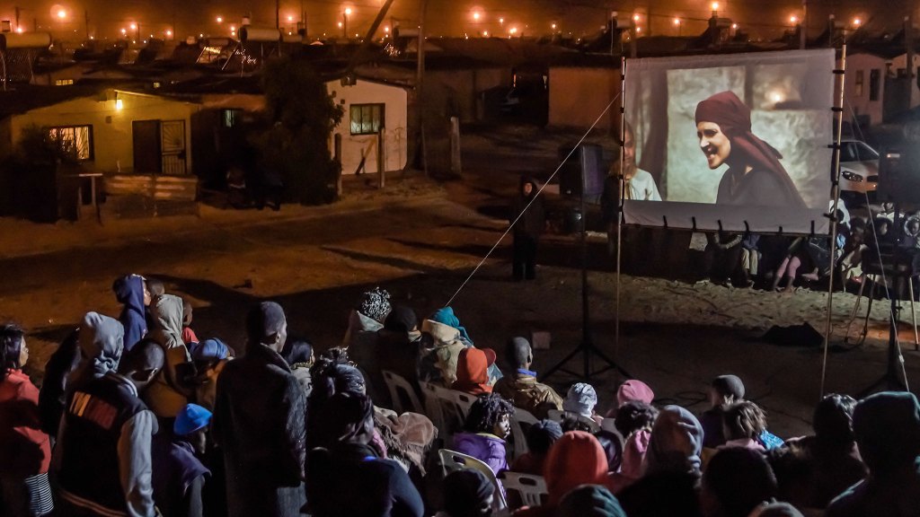 Large crowd gathered watching the Jesus Film being projected on a screen outdoors